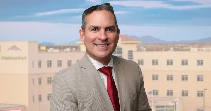 Portrait of MountainView Regional Medical Center CEO Patrick Shannon in a tan suit and red tie, with the hospital campus blurred in the background.
