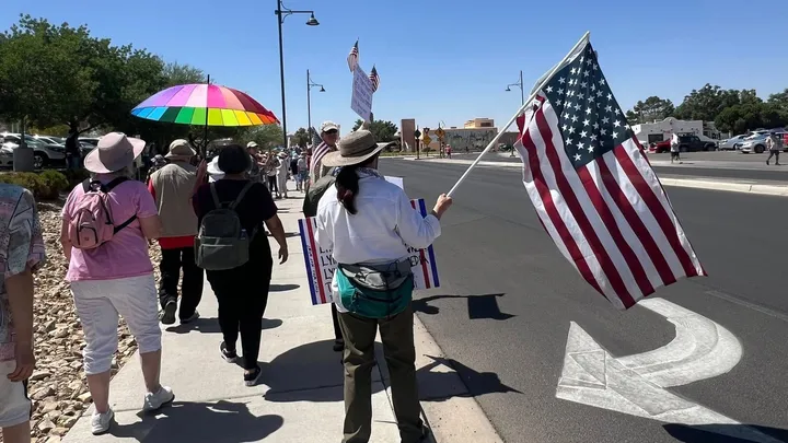 People walk along a Las Cruces sidewalk during a previous No Kings rally, carrying signs and an American flag.