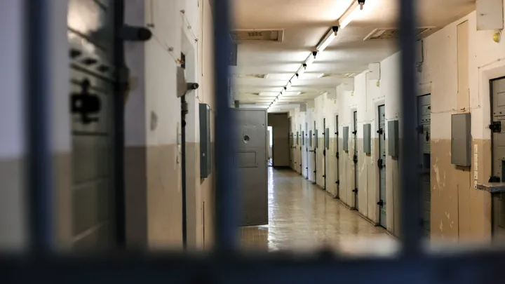 Interior view of a prison cell block corridor with rows of secured doors and barred foreground