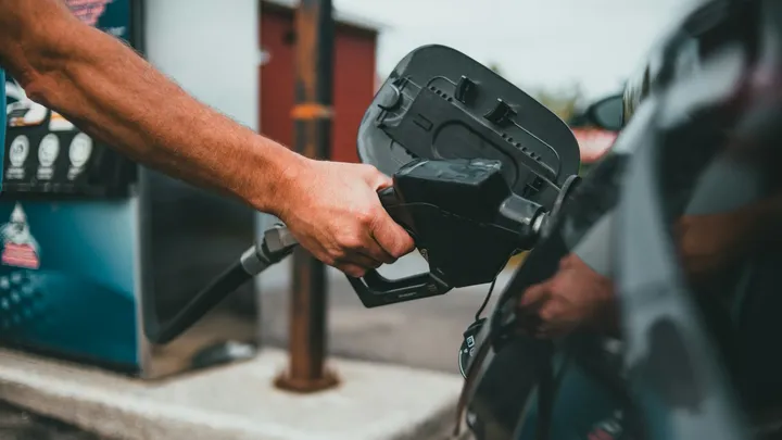 Person pumping gasoline into a car at a gas station as fuel prices rise ahead of Spring Break travel.