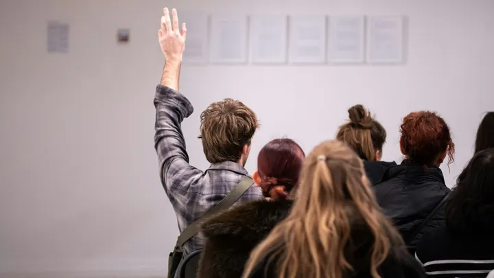 Person raises hand during in-person auction registration or bidding event with attendees seated in a room