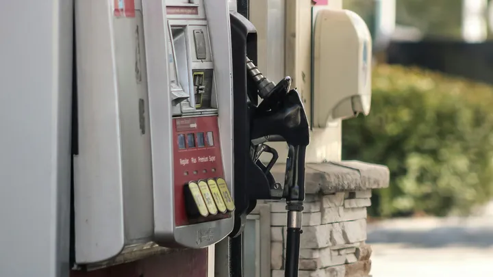 A gas pump nozzle rests in its holder at a fuel station, with price selection buttons visible on the pump.